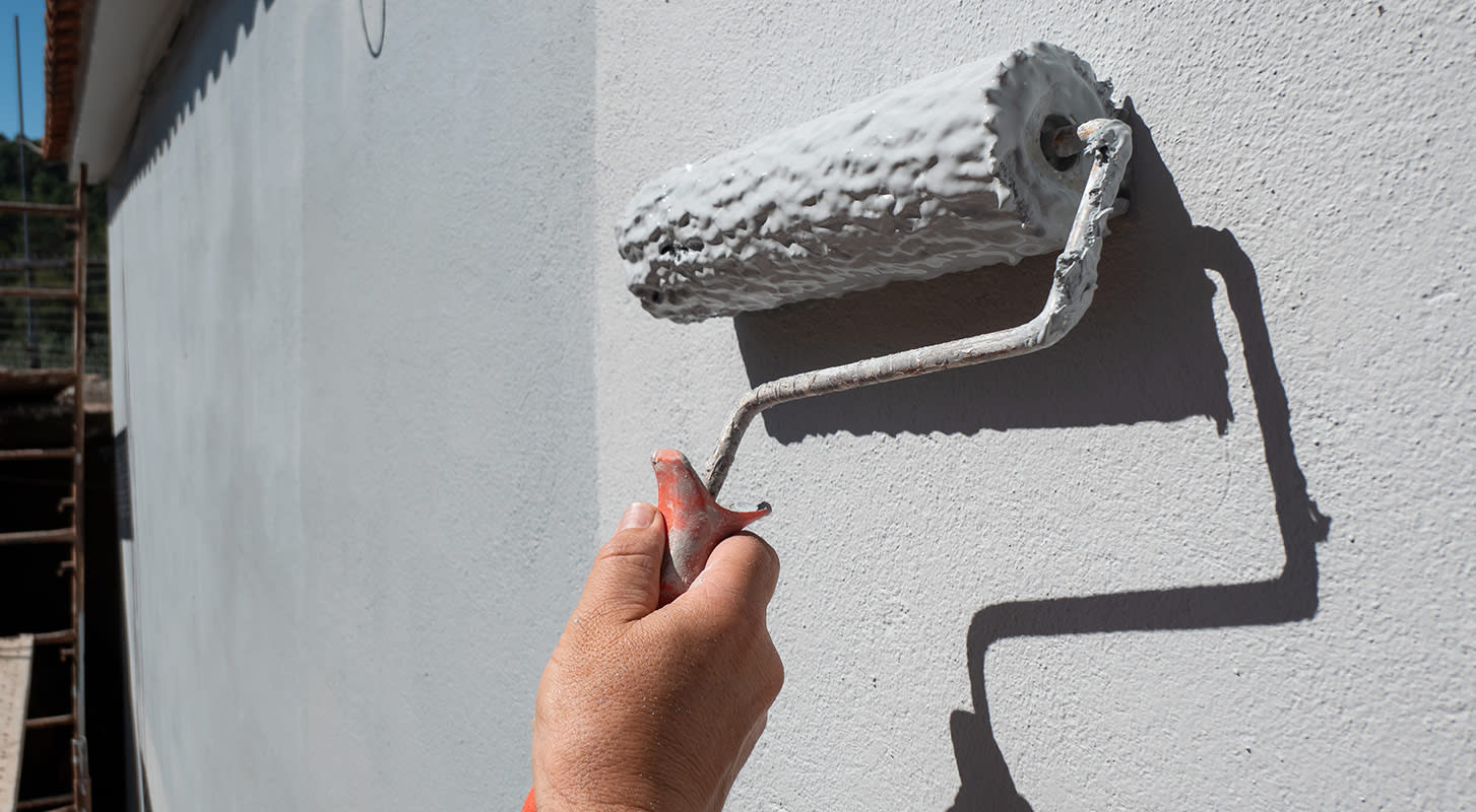An individual painting a wall with a roller.